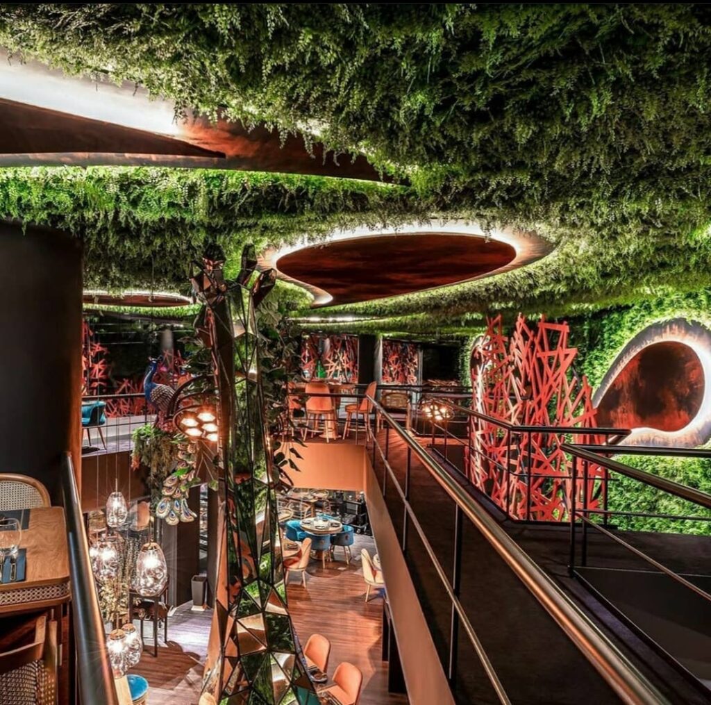Three stylish artificial potted plants in green, white, and pink pots, placed on a wooden shelf with drawers, designed by Fairy Tale Green Walls in Limassol, Cyprus.